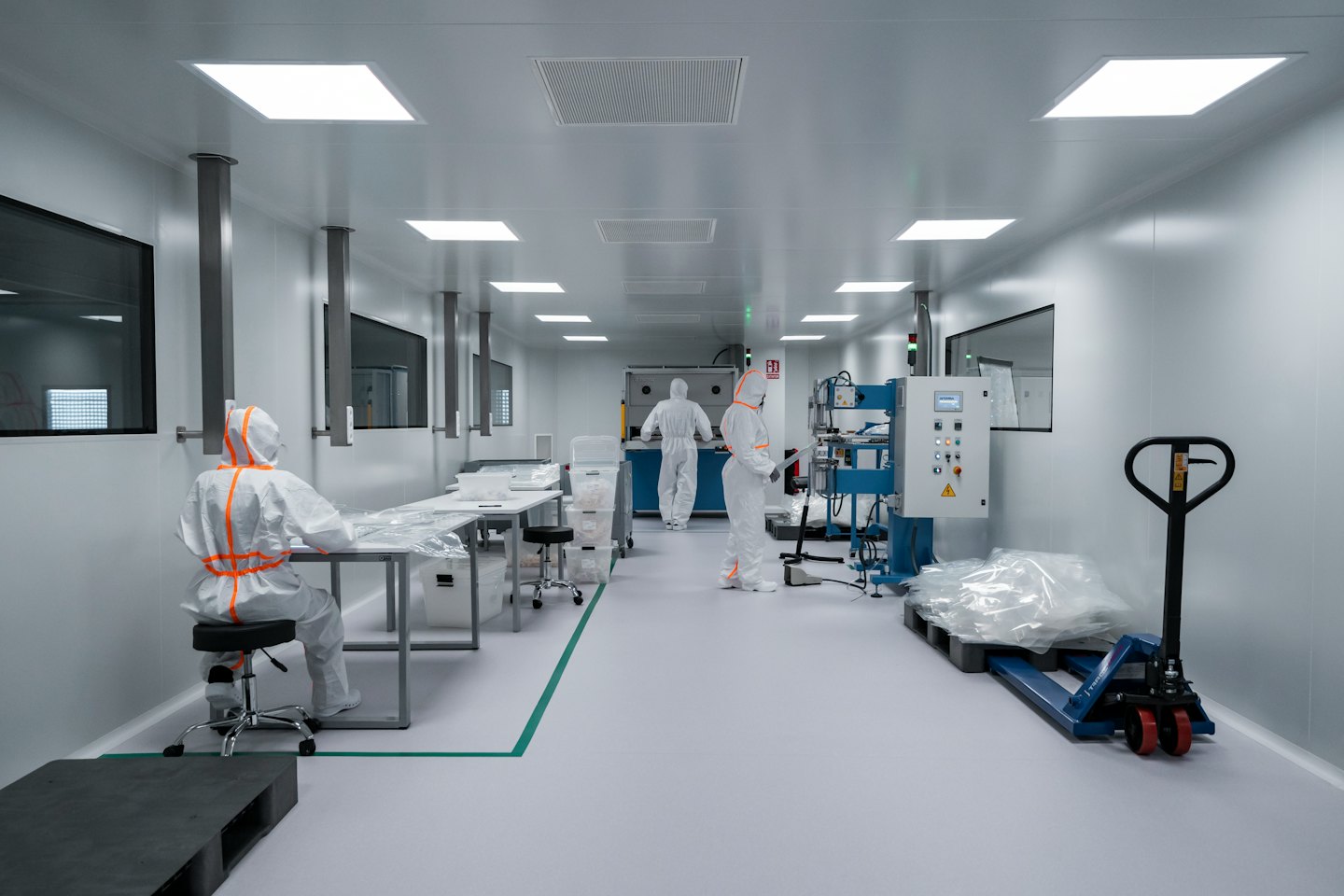 Three technicians in cleanroom suits operate equipment in a facility.